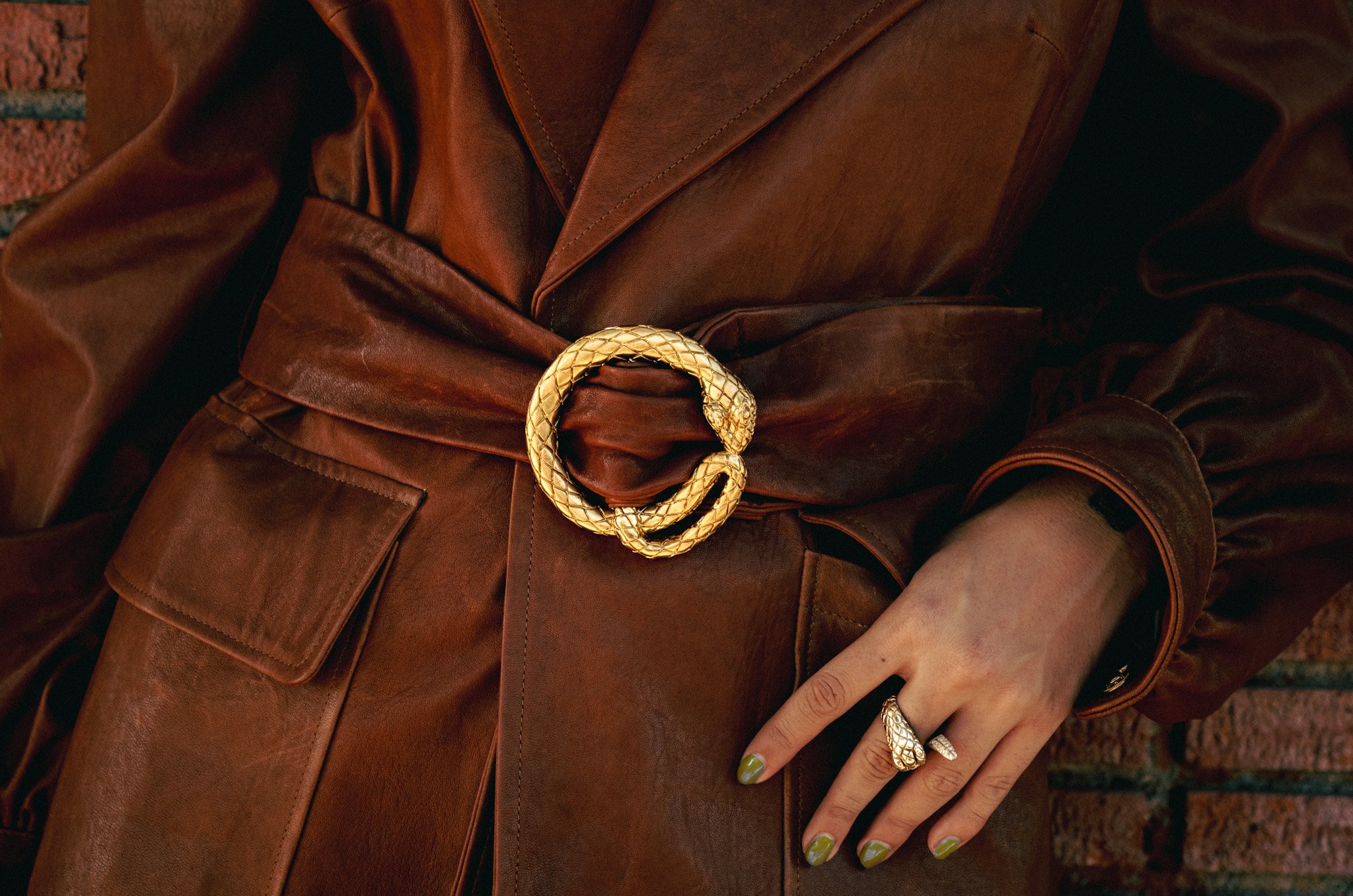 Gold ouroboros buckle on brown leather, serpent ring on hand