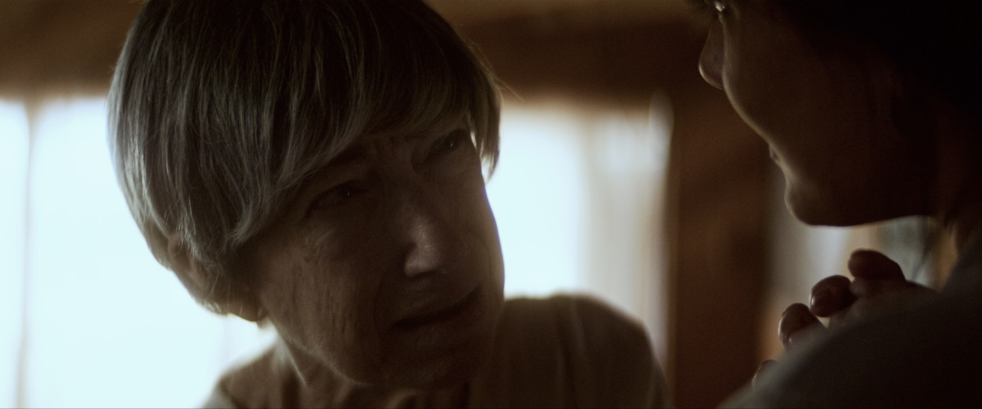 An older woman, the raw look. A hand at her shoulder.