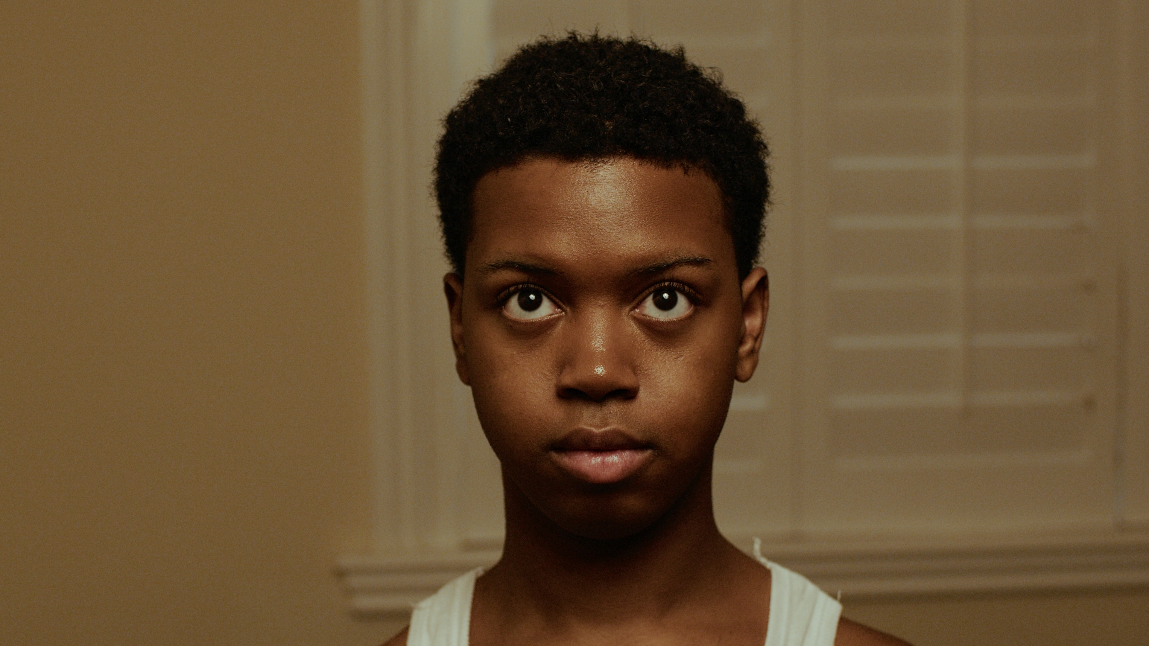 Portrait. White tank, beige walls, eyes lifted.