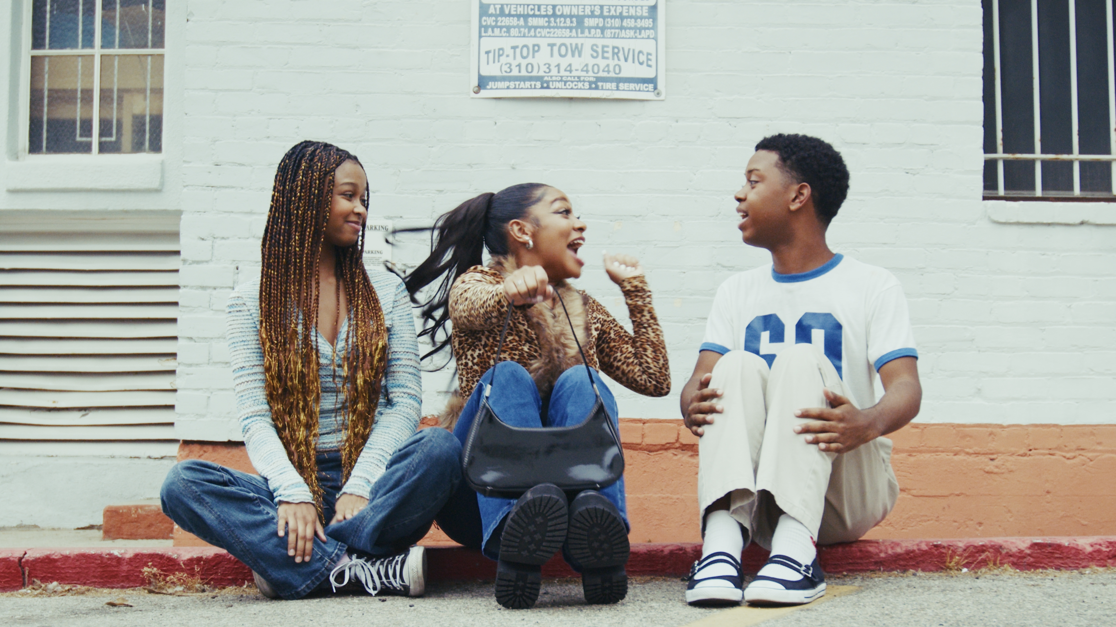 Three teens on the curb. Mid-conversation outside Tip-Top Tow Service.