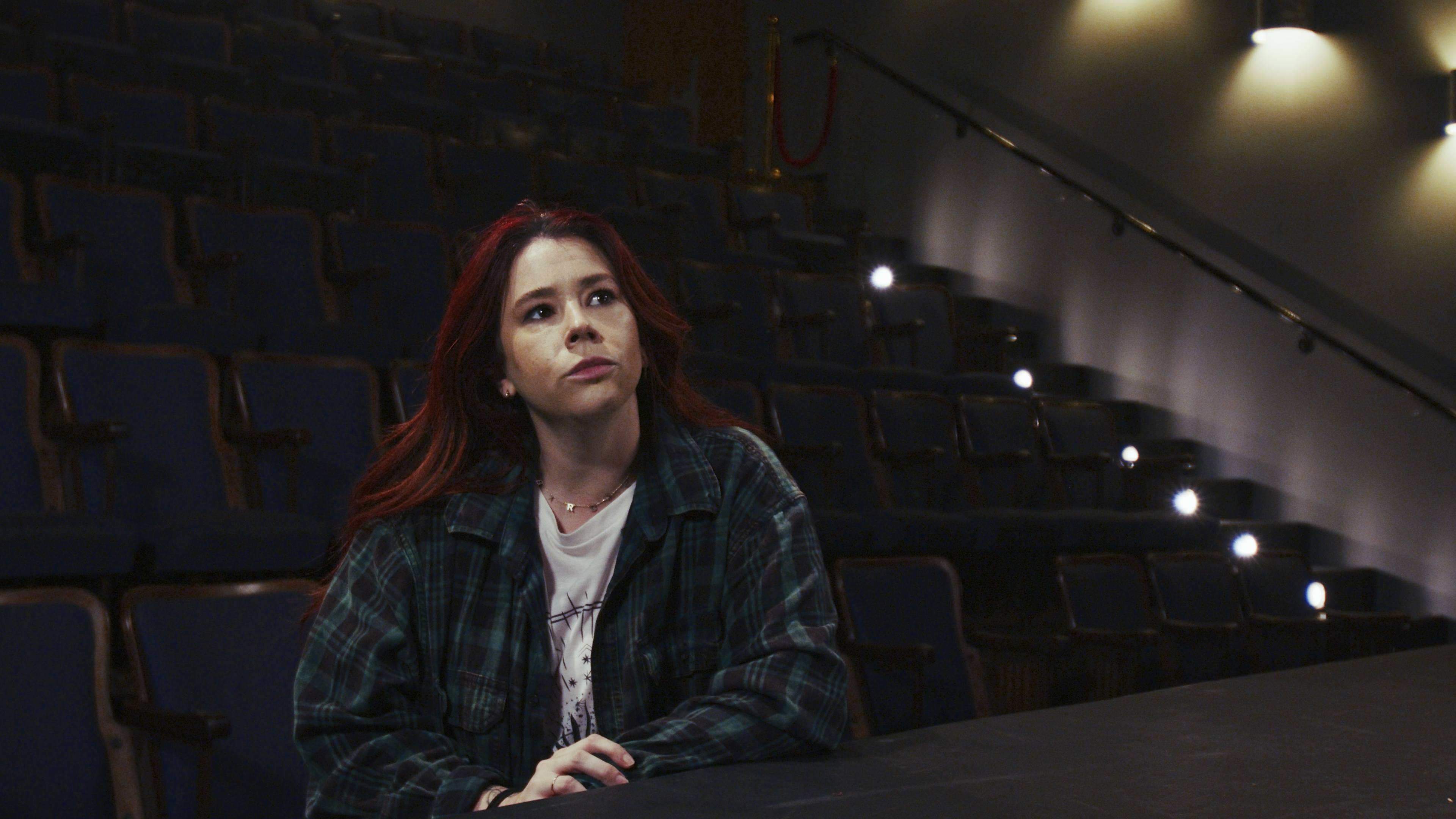 An empty theater. She sits alone.