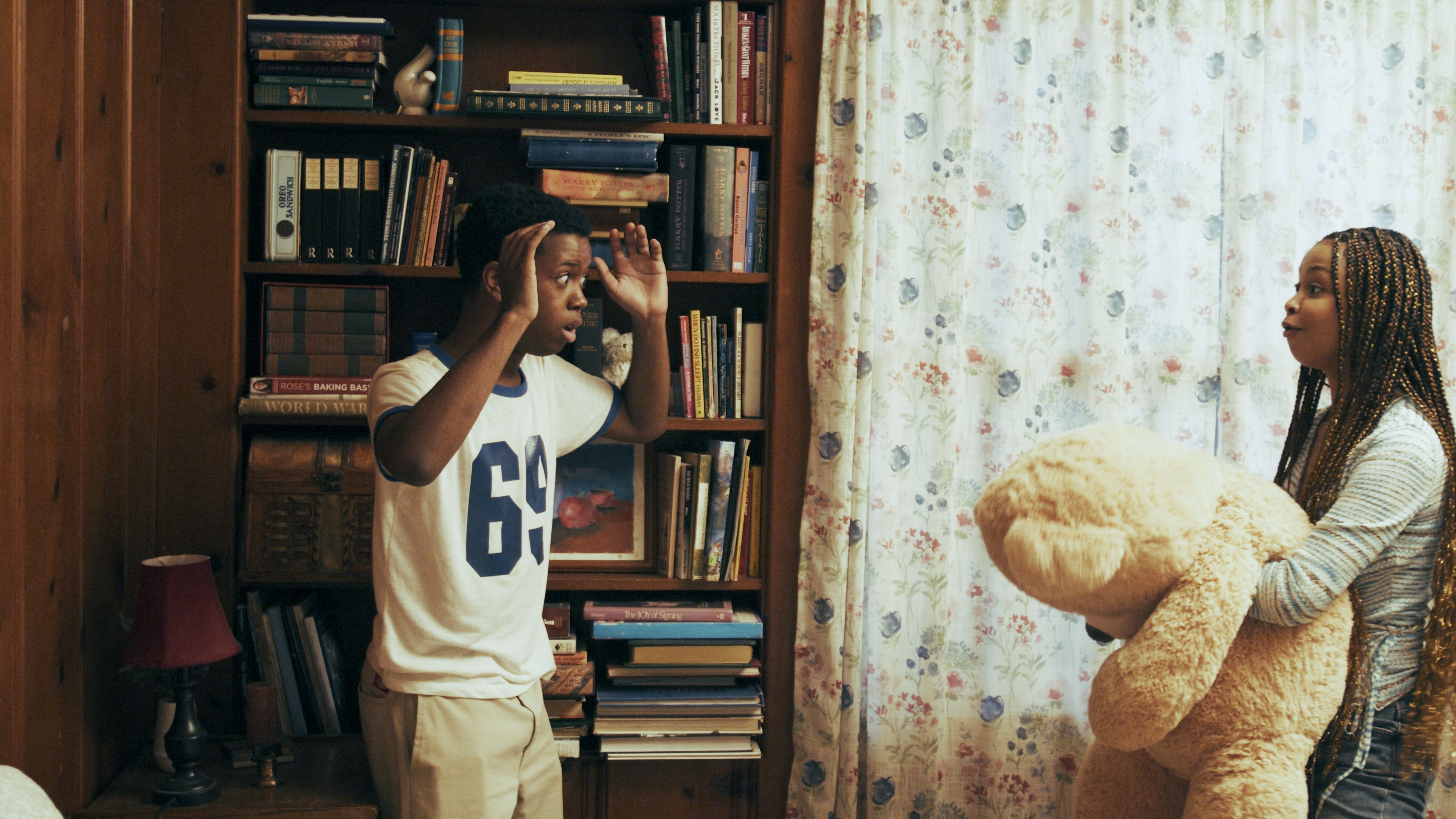 Wood-paneled room. Hands up. A teddy bear, a girl in the doorway.
