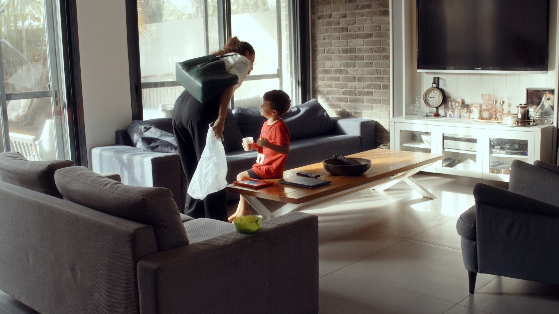 A woman leans down to a child on the couch. Living room, afternoon light.
