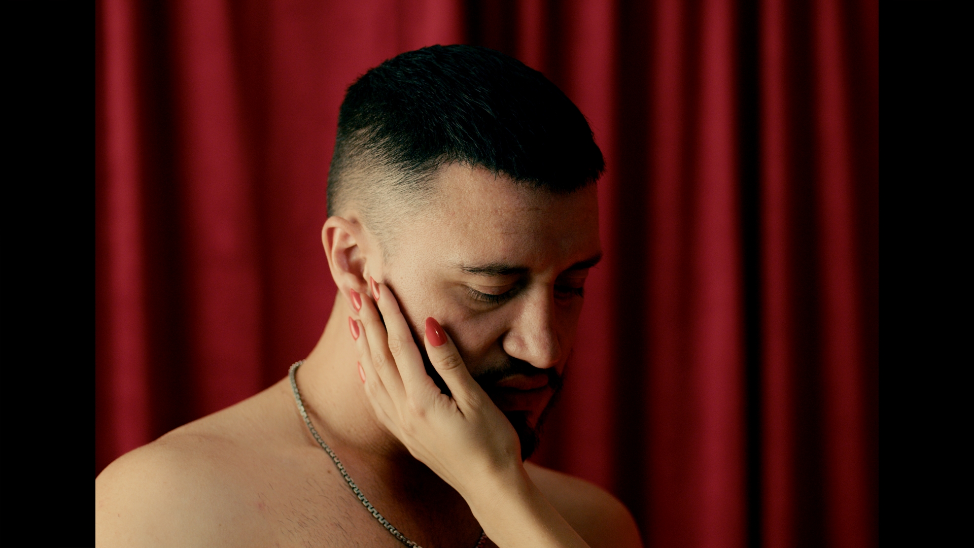 Red curtain. A hand with painted nails on his face.